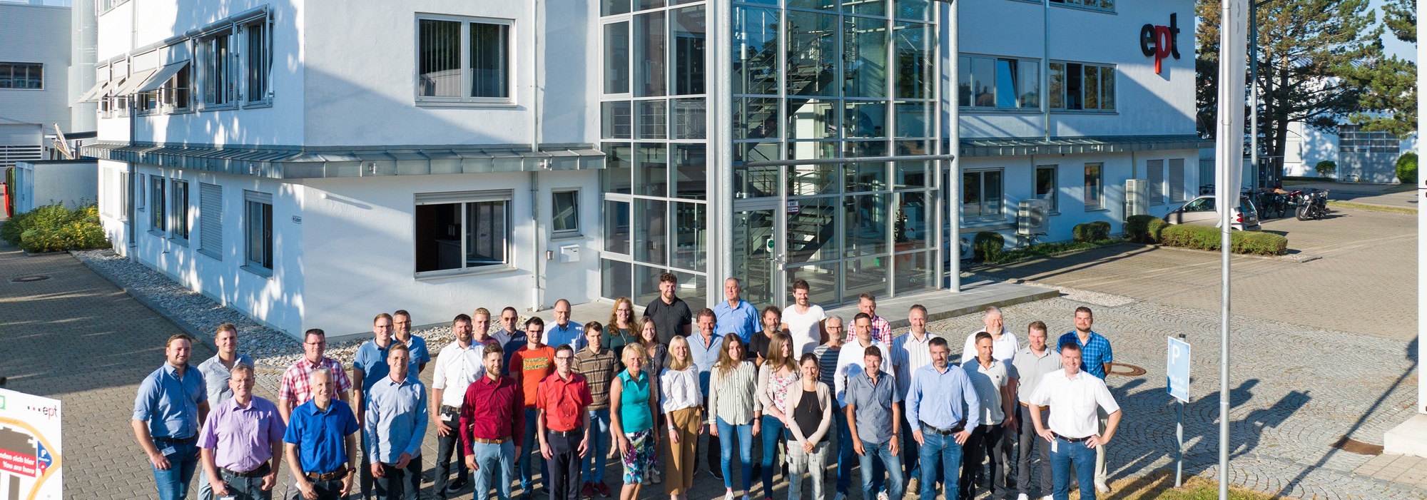 Auf dem Bild ist ein Teamfoto von Mitarbeitern vor einem modernen Firmengebäude zu sehen.